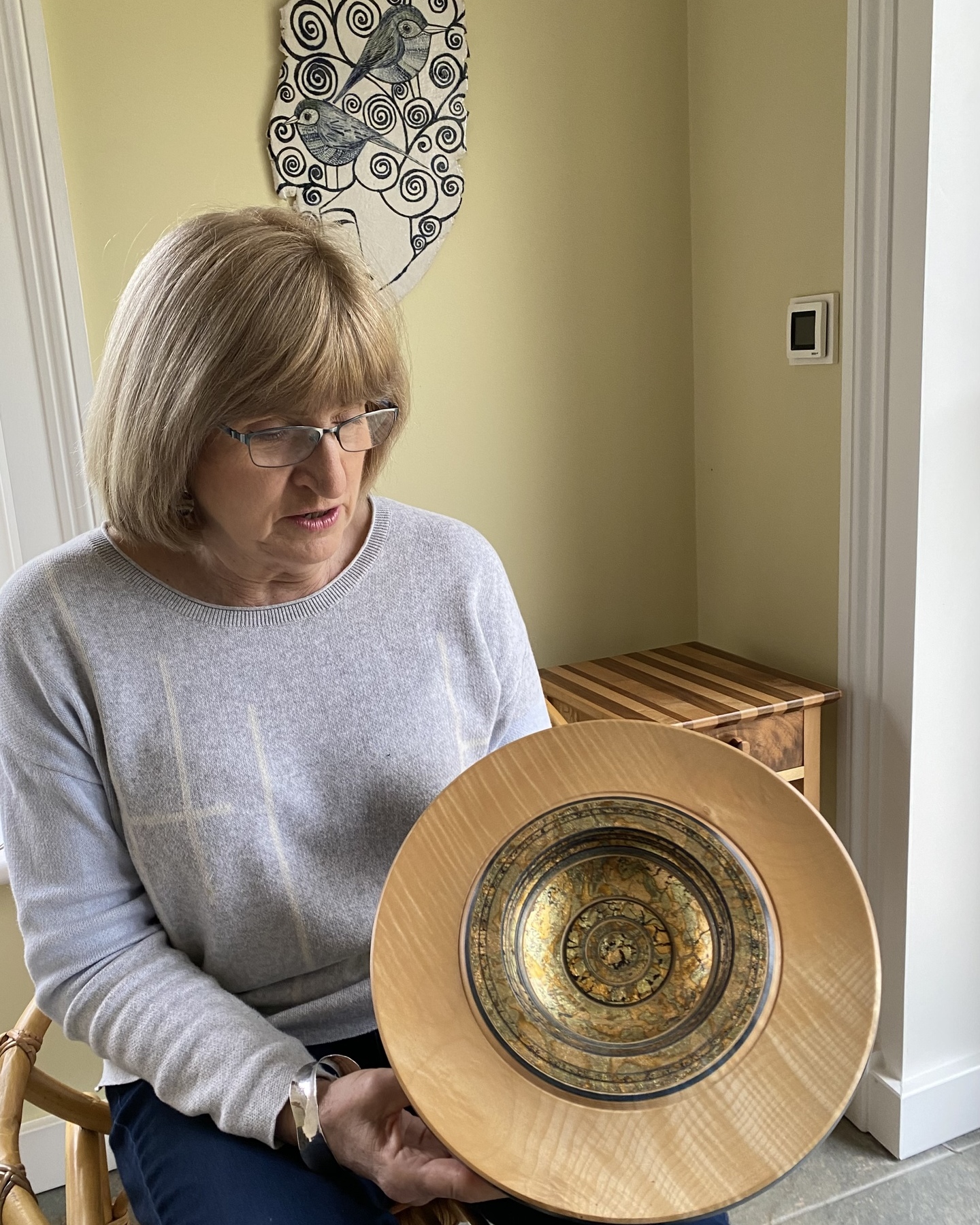 Sarah holding a plate by Dennis Hales, with furniture by Niall Craig and a plaque by former member Karen Risby in the background